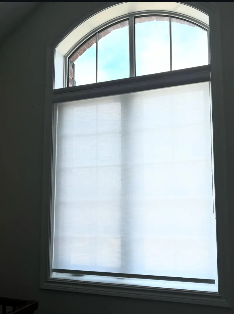 A white light-filtering roller blind on a tall window under an arched transom