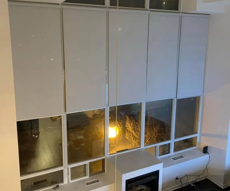 Tall white roller shades on a two-storey window wall