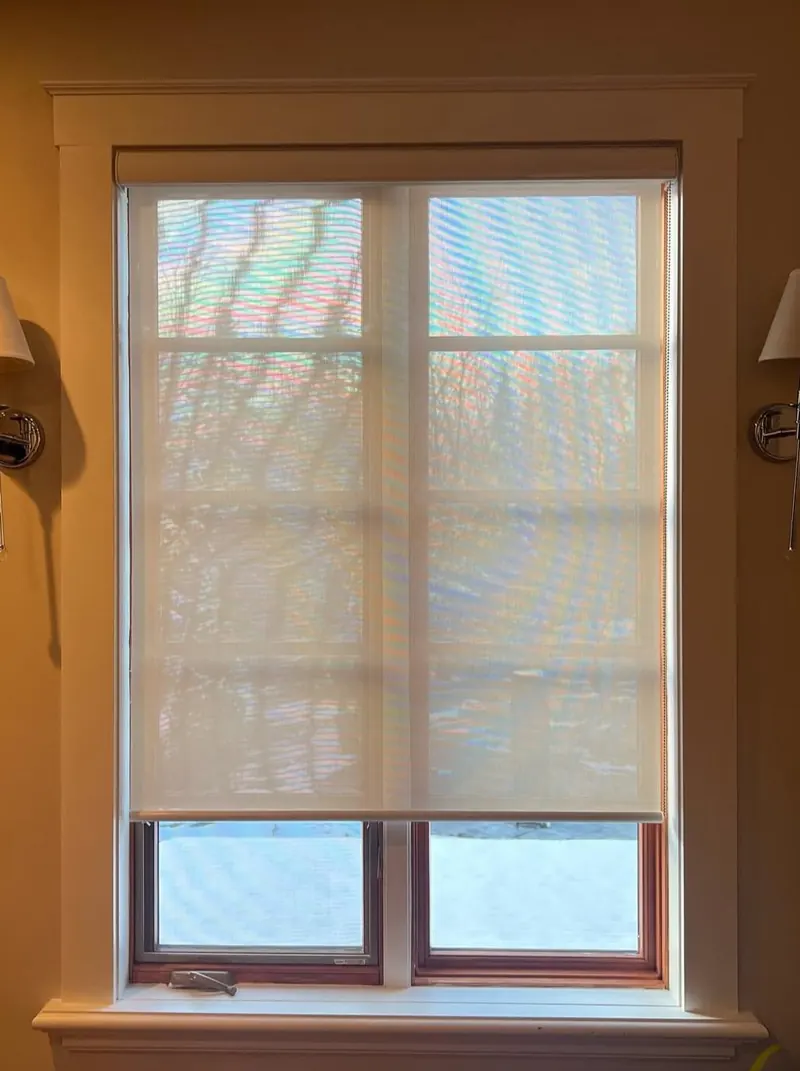 A sheer roller blind on a window with wood trim