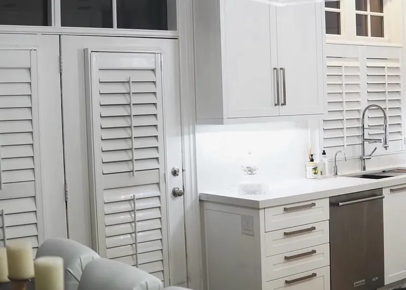 White plantation shutters on the windows and pantry door of a bright kitchen